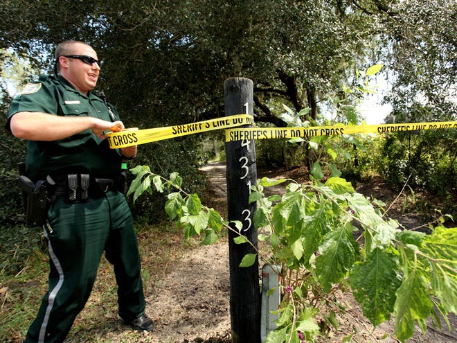 An Alachua County sheriff's deputy puts up crime scene tape to keep media away from an accident scene at 14313 S.W. 79th St. on Tuesday. Law enforcement were working the scene where two tree trimmers were injured when a rope they were using touched a power line.
