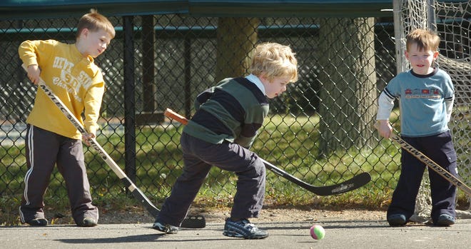 Tyler Walser, 5, hits a street hockey ball by Nolan Holloway, 5, and Gavin Holloway, 2, all of Pembroke, at a Hanover playground. Gorgeous autumn weather has folks flocking outdoors.