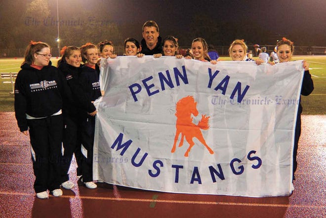 The Penn Yan varsity cheer squad poses with Doug Westerdahl behind the flag he presented to the school before the Mustangs football game Oct. 9. He and his brother, Steve, were members of the PYA class of 1975. The brothers earned varsity letters in football, tennis and track.