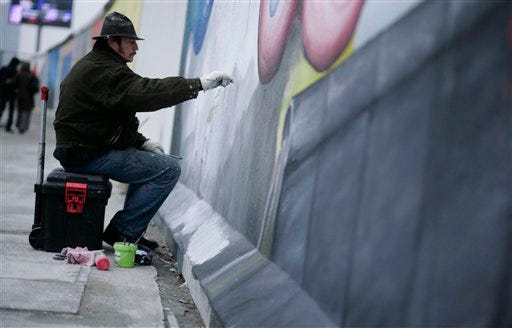 In this Oct. 21, 2009 file picture German artist Gerald Kriedner paints at his picture on a segment of East Side Gallery in Berlin, Germany. 91 artists worldwide have gathered 20 years since the wall came down on Nov. 9, 1989, to repaint their original creations on the concrete slabs, bringing new life to images that were eroded by the elements and time that had decorated the longest remaining length of the wall that once split Berlin and, to an extent, west and east. (AP Photo/Markus Schreiber)