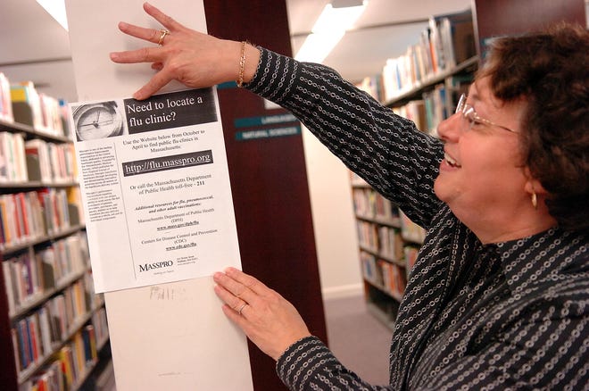 Circulation Supervisor Rebecca Hall hangs a flu information sign in the Raynham Public Library on Wednesday afternoon. At least four students at LaLiberte Elementary School in Raynham have contracted the swine flu.