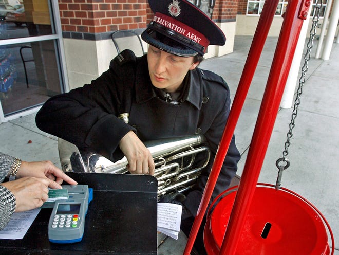 In this recent undated photo, Matt Sims, bandmaster for the Salvation Army, talks a donor through a credit card donation at the kettle he was manning at the Forest Hill Ukrop's in Richmond, Va. The charity is testing kettles that take debit and credit cards. The growth of so-called "plastic kettles" comes as fewer shoppers carry cash.
