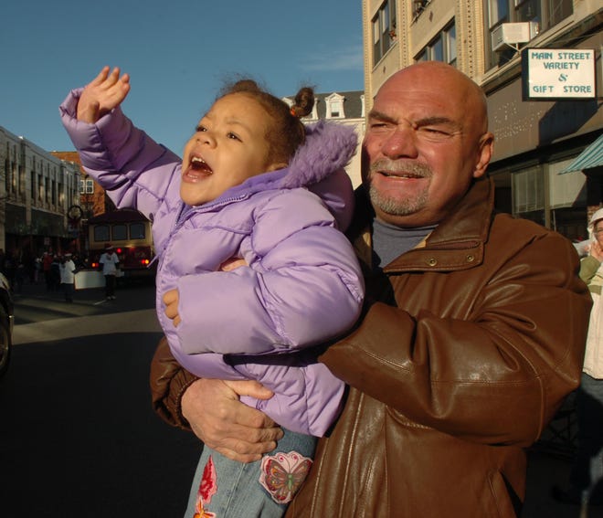 Amaria Hume, 3, of Brockton waves to Santa while being held by her grandfather David Hume of Brockton during Saturday's annual Brockton holiday parade.