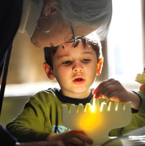 Frederick Rota, 4, of Wellesley puts colored pins on his menorah to represent flames as his grandmother, Susan Fasten of Millis, watches yesterday during the Community Hanukkah Celebration at MetroWest Jewish Day School in Framingham.