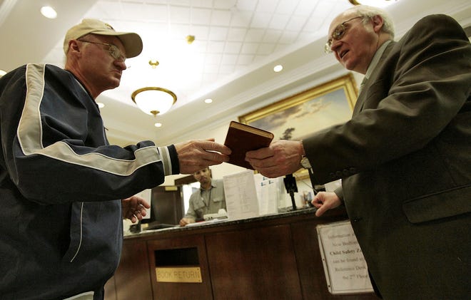 Stanley Dudek, left, returns a book that was 99 years, seven months and 12 days overdue to New Bedford, Mass., library director Stephen Fulchino, right, Monday, Dec. 14, 2009. Dudek returned it on behalf of his deceased mother after he found it among her belongings.