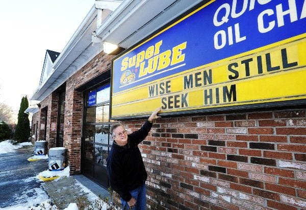 Russell Texeira puts up positive phrases on the sign in front of his Super Lube store on Main Street in Falmouth.