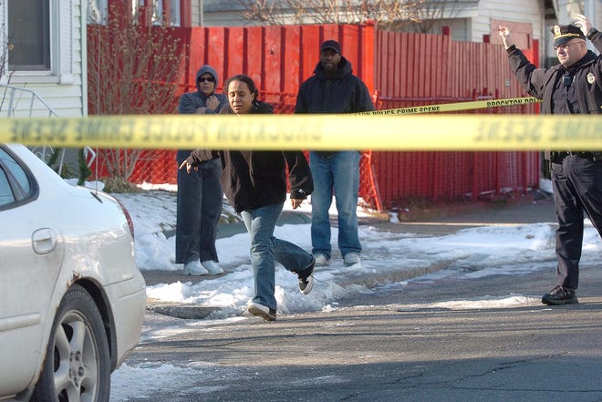 A distraught woman runs by police and enters the crime scene in front of the house at 52 Nilsson St., Brockton, where the bodies of a brother and sister were found shot to death Thrusday morning.