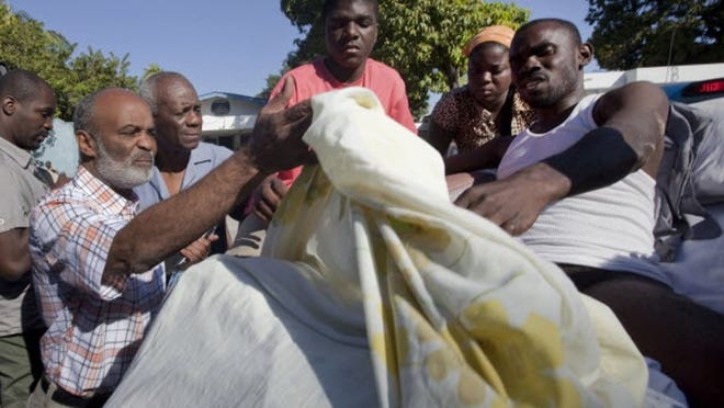 Preval, left, looks at the wounds of an earthquake survivor in Port-au-Prince.