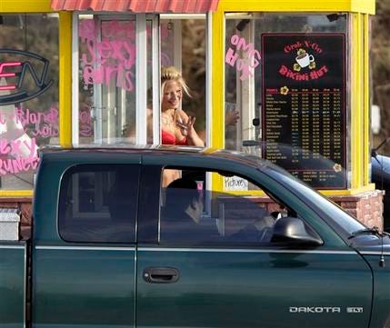 A barista at a Grab-N-Go Bikini Hut espresso stand holds money as she waves to a customer, Tuesday, Feb. 2, 2010, just outside the city limits of Everett, Wash., in Snohomish County.