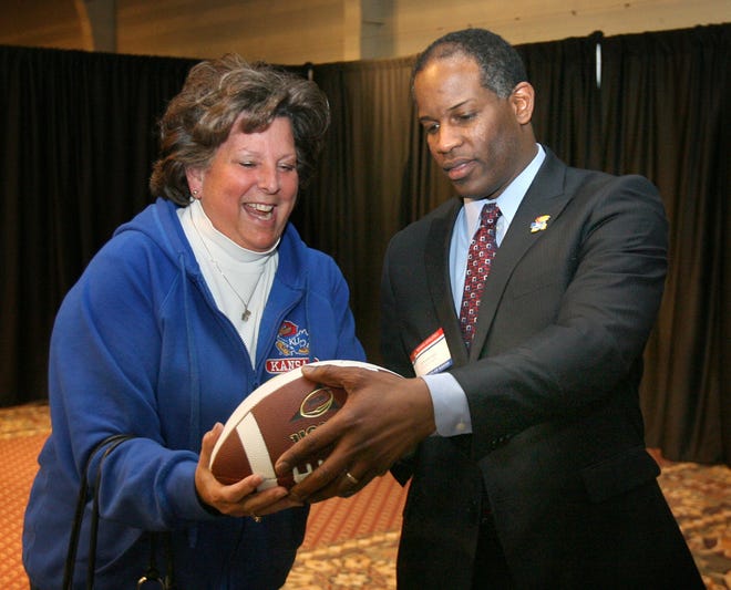 Margo Leonard, Topeka, left, received an autographed football from the new Kansas football coach Turner Gill after Gill drew her name from a box of contestants at the Topeka Jayhawk Club meeting Monday night at the Capitol Plaza Hotel Maner conference center.