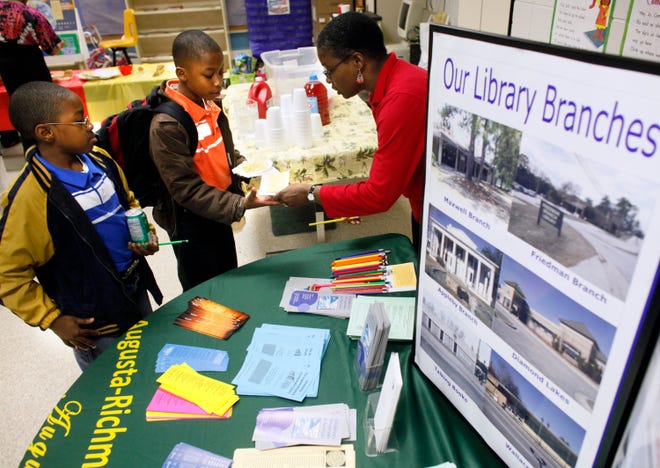 Dontavius Furgson (left) and Jonathan Butler, both 10, sign up for library cards from community service librarian Sherryl James during the opening of the Family Literacy Center at Collins Elementary School. The center will provide resources for parents to help pupils.