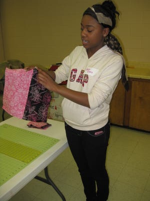 Candice Banks, 17, a Junior Ambassador in Girl Scouts, holds up two strips of fabric pieced together before she cut them into separate 13-by-13-inch blocks for the top of a quilt she is making for children victimized by the earthquake in Haiti.