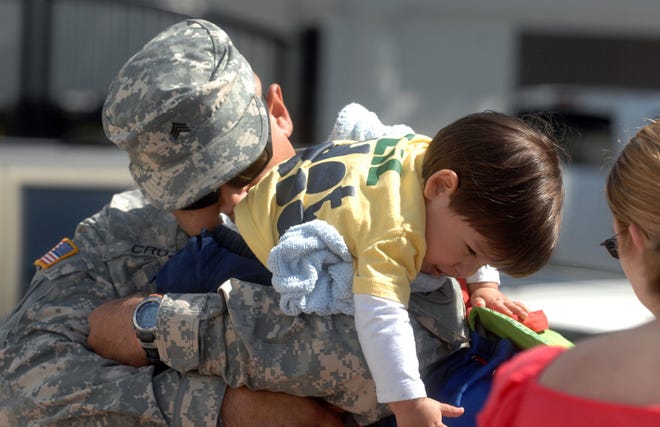 Sgt. Julio Cruz gives his son Alex, 15-months-old, a hug as his wife Brandy looks on following the Georgia National Guard 1/118th Field Artillery Regiment\u2019s flag ceremony in Forsyth Park. (Steve Bisson/Savannah Morning News)