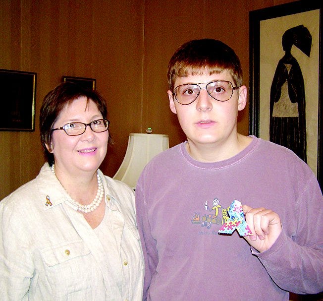 Charlie Morgan holds an autism ribbon which he and his siblings began making 10 years ago. His mother Shari Morgan wears a lapel cloisonne Autism Awareness Pin designed from the family’s trademark pattern. All proceeds benefit the Autism Society of America.