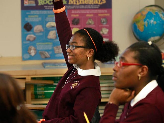 Seventh-graders at Trinity Catholic Academy, Nithaelle Simoly, left, and Angela Osiris, right, participate in science class at the school in Brockton. Simoly, who lost 11 family members in the January earthquake in Haiti, often helps Osiris with translating French to English and back while completing school work.