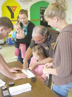 mersyn Nelson, 3, makes a set of fingerprints with the help of Chief Deputy Jim Padilla of the Henry County Sheriff’s Office, Kewanee Auxiliary Police Officer Matt DeClercq, left, and Linnea Hepner of the Kewanee King Pins 4-H Club, right.