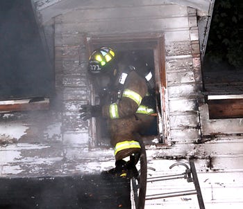 Firefighters climb through a small window to get to a fire in the attic of a home at 68767 Theodore St. in Mottville Friday night.