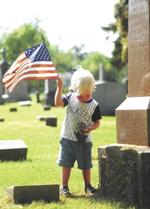 Two-year-old Hayden VaNest of Sturgis places a flag on a soldier’s grave Thursday night at Oaklawn Cemetery in Sturgis. Many groups, including Daughters of the American Revolution and Girl Scouts, helped with the placing of the flags.