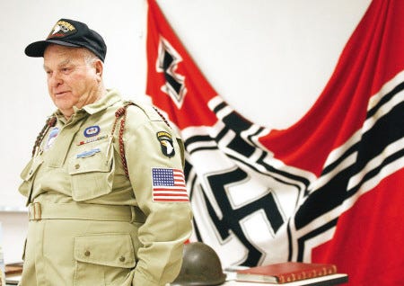 Battle of the Bulge veteran John C. Primerano, of Exeter, talks with seventh-graders at the Cooperative Middle School in Stratham about his experiences in World War II. Behind Primerano is a captured German war flag.