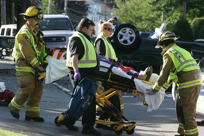 Milford fire officials transport a woman to the ambulance which took her to Milford Regional Medical Center after her car rolled over in front of 104 Purchase St. in Milford Tuesday evening.