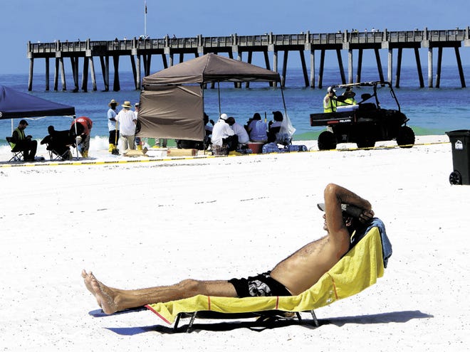 Ray Weigle of Pensacola sunbathes a hundred yards from the surf and well back from a yellow police tape banning swimmers from the public beaches in Pensacola Beach, Fla., Thursday, June 24, 2010. Oil from the Deepwater Horizon disaster continues to wash ashore along the Alabama and Florida coasts.