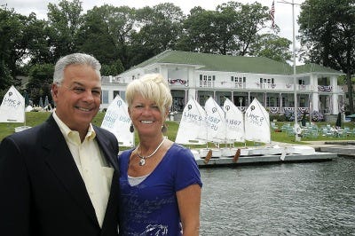 Photo by Anna Murphey/New Jersey Herald George Malanga, chairman of the Lake Hopatcong Yacht Club’s centennial celebration, and his wife, Jill, stand on a dock in front of the 100-year-old clubhouse, which is dressed up for the occasion.