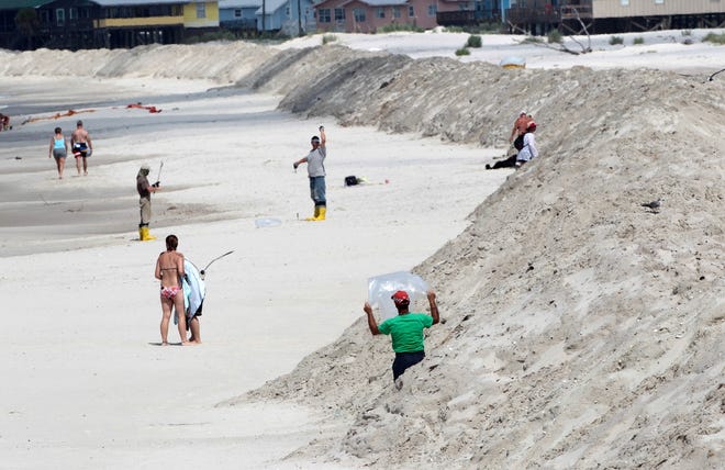 Oil cleanup crew members work Sunday next to a 10-foot berm that was built 
on the beach in Dauphin Island, Ala. AP PHOTO / DAVE MARTIN