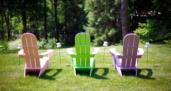 Three Adirondack chairs painted in pastel colors sit on a Pembroke lawn along the North River.