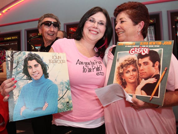 Lisa Bower of Citrus Springs, left, and her mother, Valerie Bower of Crystal River, show off their “John Travolta” and “Grease” albums as they stand in line with other people while waiting for the start of the first “Grease: Sing-A-Long” movie at the Regal Entertainment Hollywood 16 on Southwest 27th Avenue in Ocala on Thursday. The showing was the first of six shows sold-out shows at the theater.