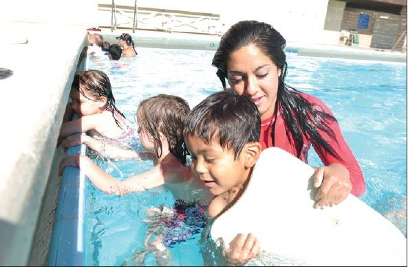 LESSONS: Swimming instructor Christina Umara, 19, gives a swimming lesson to Alekander Barajas, who's holding onto a floating pad, and other students at Pebble Beach Pool at Doris Davies Park in Victorville on Monday.