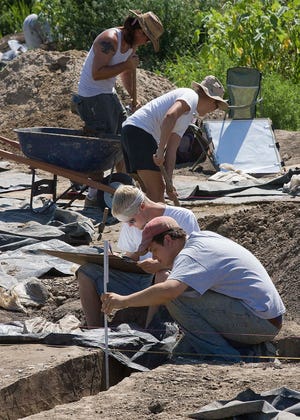 In this photo taken July 16, 2010, Casey Langenstein, seated left, of Collinsville, Ill. takes down readings as Matt McGuire, seated right, of Madison, Wis., checks the depth of the excavation going on at the site of a massive archaeological dig now under way at the old National Stock Yards in National City, Ill. A 6-inch-high figurine uncovered at the construction site of a new $670 million Mississippi River bridge has caused great excitement among archaeology professionals and students. (AP Photo/Belleville News-Democrat, Tim Vizer)