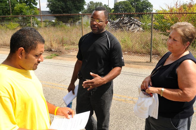 Antonio Godoy gets a handout from State Rep. Harold Mitchell and Spartanburg County Council member Jane Hall about a planned meeting to discuss the cleanup efforts at the abandoned Victor Mill in Greer.