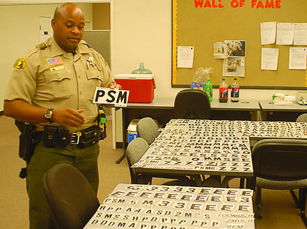 San Bernardino County Sheriff's Deputy Rick Polidore stands among a cache of graffiti materials at the Barstow Sheriff's Station on Friday morning. The items were recovered when three men suspected of causing graffiti were arrested early Friday morning in Yermo.