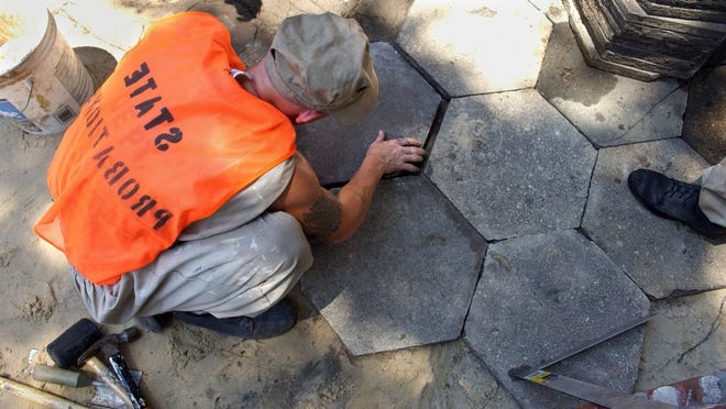 An inmate from a probation detention center in Alma, with his safety vest inside out, places pavers on a sidewalk.