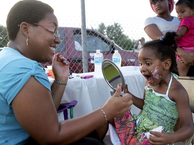 Tasia Green, 5, reacts with delight at her face painting while painter Amour Jenkins holds a mirror Tuesday evening during the Annual Night Out Against Crime.