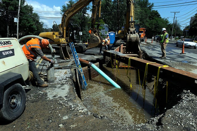 Workers pump water out of a giant hole on A Street at Concord Street Friday after a water main break briefly flooded the area during road construction.