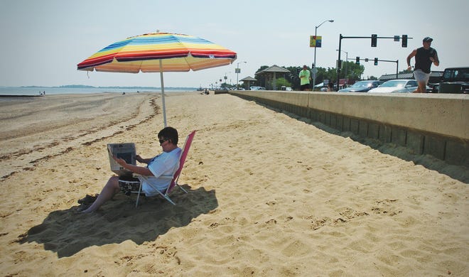 Catherine Bradfield reads while sitting under a beach umbrella at Wollaston Beach in Quincy on Saturday.
