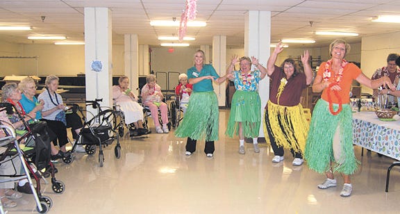 In honor of Hawaii’s becoming a state in August 1959, employees and residents enjoyed Hawaiian-themed activities Friday. Employees, from left, are Dawn Russell, Marilyn Pritchard, Barb Tolbert and Shelah Gaston demonstrate the hula with plastic grass skirts and leis, while residents look on. Also offered were Hawaiian foods such as pineapple and coconut cake with edible orchids, Hawaiian music and games.
