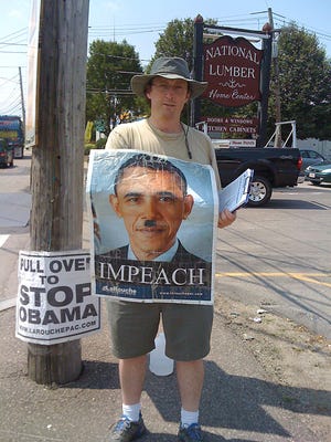 A campaign worker for Congressional candidate Rachel Brown wears a poster depicting President Barack Obama with a mustache similar to that worn by Adolph Hitler.