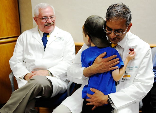 Surgeon Venkataraman Ramachandran, right, gets a hug from Ethan as Ted Groshong, left, watches after the news conference Wednesday.