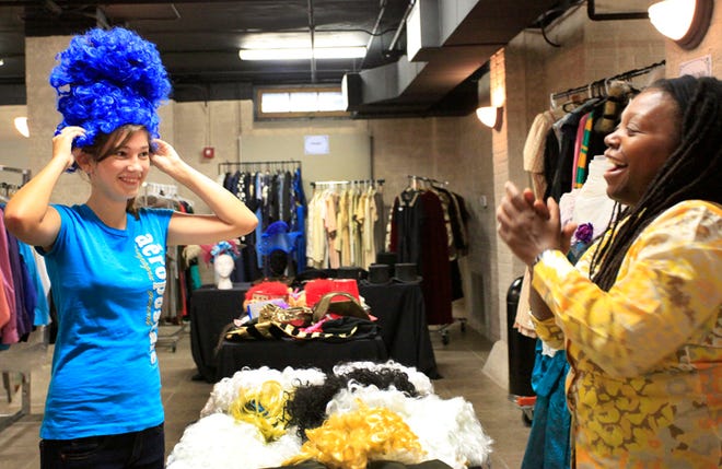 Gabrielle Byam laughs as Brooke Utter, 12, tries on a wig for sale at the Hippodrome State Theatre's Costume Fashion Show before selling them in an auction Saturday.