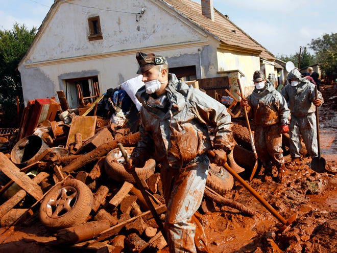 Hungarian soldiers clean a yard flooded by toxic mud in Devecser, Hungary, Thursday, Oct. 7, 2010. The toxic red sludge that inundated three Hungarian villages reached Europe's mighty Danube River on Thursday but no immediate damage was evident, Hungary's rescue operations agency said. The European Union and environmental officials had feared an environmental catastrophe affecting half a dozen nations if the red sludge, a waste product of making aluminum, contaminated Europe's second-longest river after bursting out of a factory's reservoir. (AP Photo/Darko Bandic)