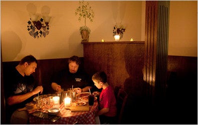 A family eats by candlelight at a restaurant in Salina, Kan., part of an effort to conserve power.