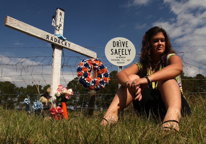Reece Griffis, 16, sits beside a homemade cross and a highway marker in memory of her boyfriend Theodore Julius “T.J.” Radacky on State Road 121 in Williston. Radacky died June 15 after he was ejected from his vehicle after it struck a telephone pole and rolled. He was 16.