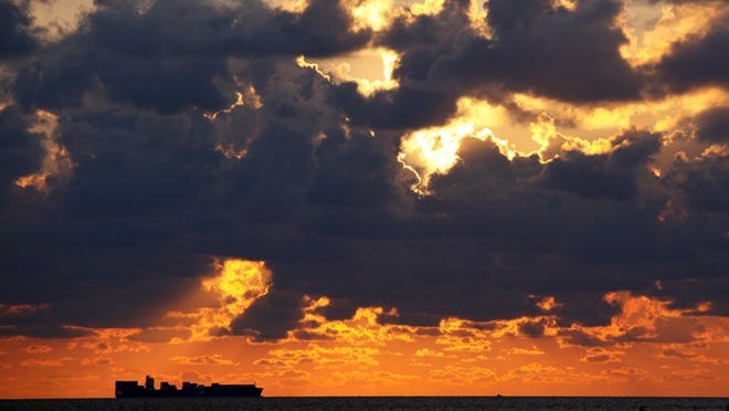 The sun rises over a container ship passing Lake Worth Municipal Beach Friday morning. Despite the clouds, only a 10% chance of rain is forecast for today.