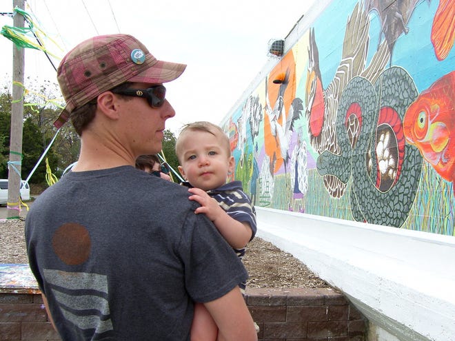 Zach Snethen, holding his 10-month-old son Oliver, checks out the latest addition to the Great Mural Wall of Topeka after a ceremony Saturday afternoon at the mural site, near S.W. 20th and Western.