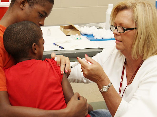 Adam Roberston, 15, holds his brother David Robertson, 6, as Donna Richardson, a RN and immunization manager for Public Health Area 3, gives David a flu shot at an annual mass flu shot clinic hosted at the Belk Center inside Bower's Park Monday.