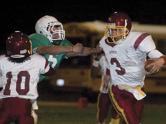 Barstow quarterback Steven Deverell, 3, runs as Victor Valley's Zeke Julien grabs his jersey and Ricky Burns blocks during the annual Axe Game on Friday in Victorville.