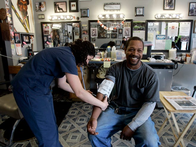 Dwight Woods, right, smiles as nursing student Meghan Welsh takes his blood pressure at Flotrin’s Barber Shop in St. Louis. In several cities, health workers are going to barbershops, long a gathering place for black men, to provide screenings to those who may not get regular checkups.