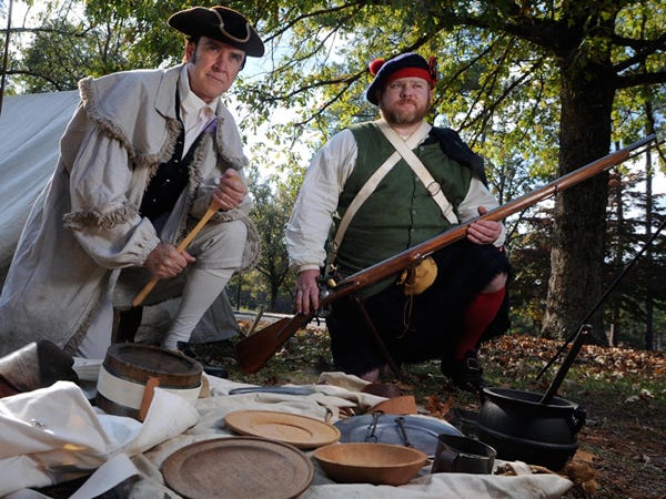 Moores Creek National Battlefield guides Terry Mitchell (left), representing a patriot in the Revolutionary War, and Jason Howell, representing a loyalist during the Moores Creek Battle, kneel behind items that would be found in a Revolutionary War soldier’s haversack.